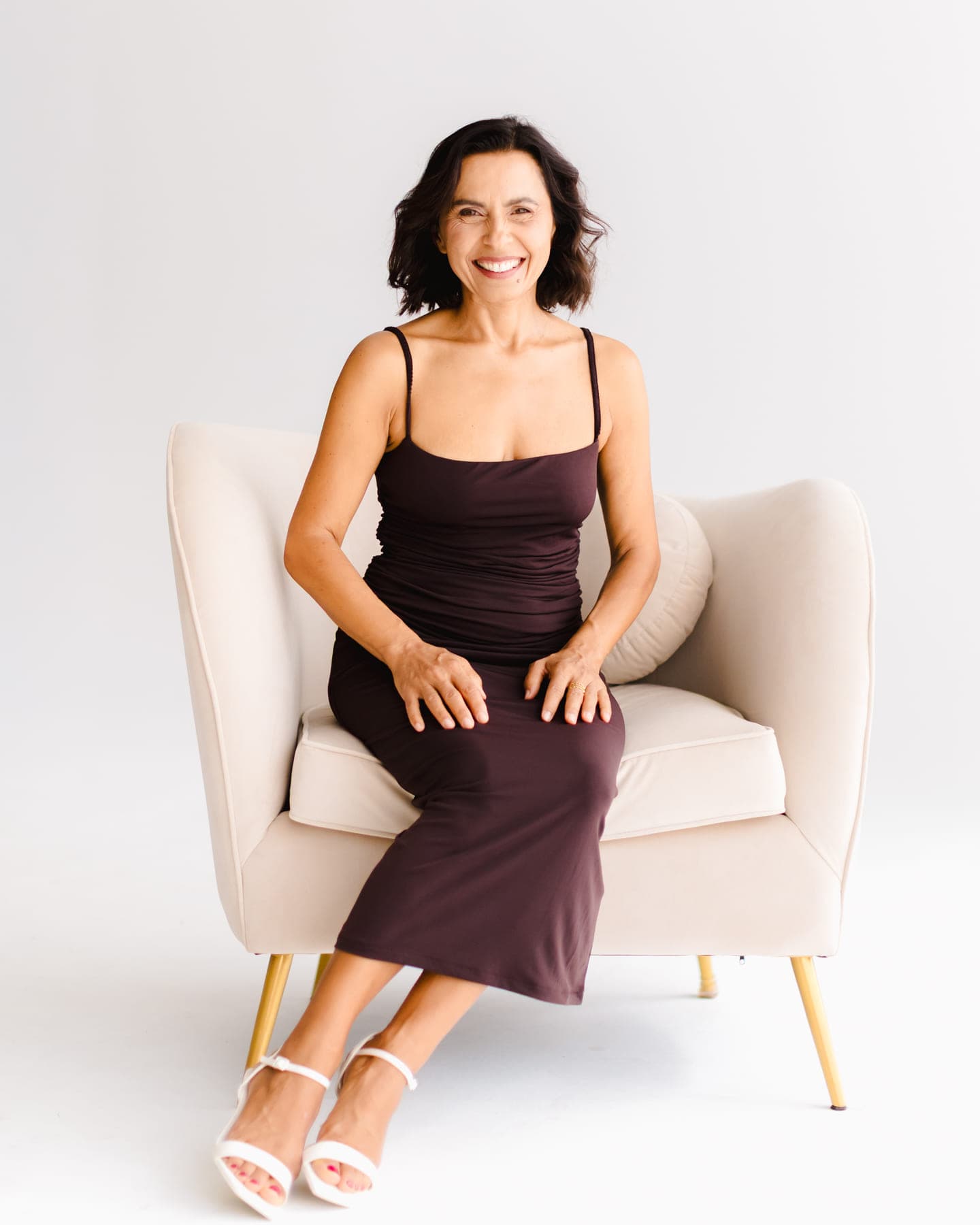 Sónia Brito numa poltrona creme, de vestido cor de ameixa, a sorrir para a câmara.
